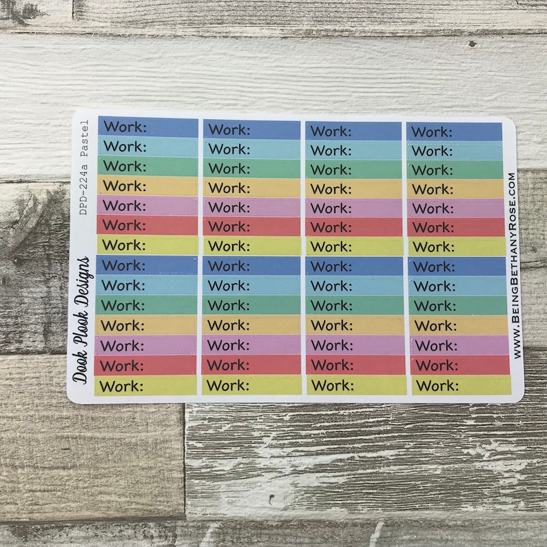 Op de afbeelding: Een vel met kleurrijke planner stickers met het woord "Work:" herhaald op elke sticker. De stickers zijn in een regenboog van kleuren, waaronder blauw, groen, geel, oranje, roze en rood.