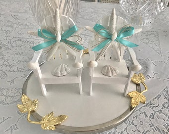 May include: Two white miniature chairs with starfish and blue bows on top, sitting on a silver tray with gold leaf accents.