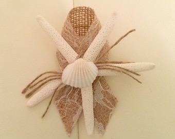 May include: A decorative ribbon featuring a seashell and starfish design. The ribbon is made of burlap and lace, with white starfish arranged around a central seashell. Jute twine adds detail to the design.