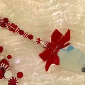 May include: A silver cake server with a red velvet bow and a handle decorated with red and white candy cane beads.