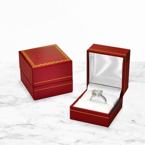 May include: Two red ring boxes. One box is open and shows a white ring with a clear stone inside. The box is lined with white satin.