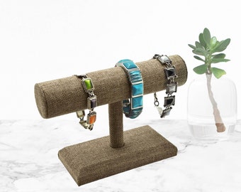 May include: A brown burlap jewelry stand with three bracelets. The bracelets are turquoise, green, and black with silver accents.