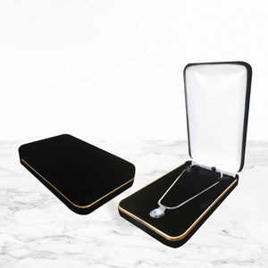 May include: Black velvet jewelry box with gold trim, one open to display a silver necklace with a teardrop-shaped pendant. The box is lined with black velvet and has a white interior lid.