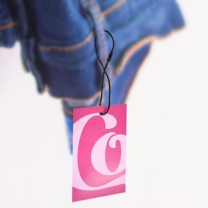 May include: Pink clothing tag with a white stylized letter C.