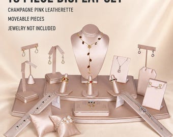 May include: An 18-piece jewelry display set in champagne pink leatherette. The set includes a necklace bust, earring stands, ring cones, bracelet ramps, and display pillows. Text reads: 18 PIECE DISPLAY SET, CHAMPAGNE PINK LEATHERETTE, MOVEABLE PIECES, JEWELRY NOT INCLUDED.