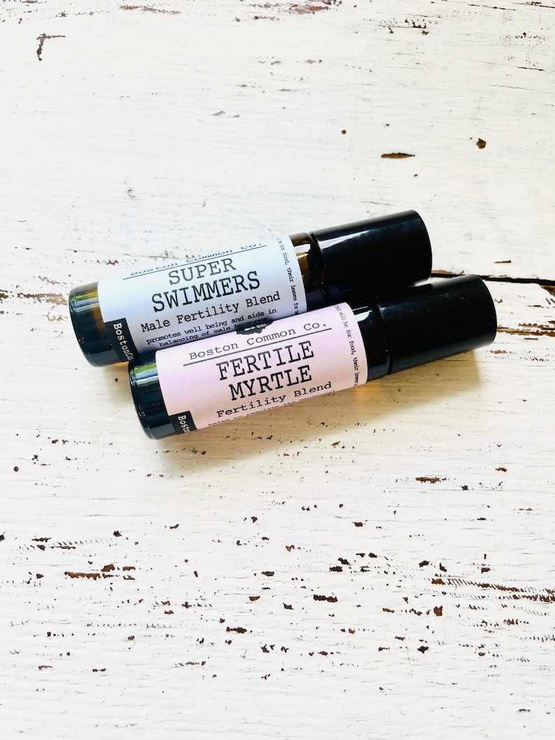 May include: Two small brown glass roller bottles with black caps. The bottle on top has a white label with the text "SUPER SWIMMERS Male Fertility Blend" and the bottle on the bottom has a pink label with the text "FERTILE MYRTLE Fertility Blend".
