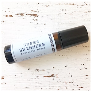 May include: A brown glass roller bottle with a black cap and a white label that reads "SUPER SWIMMERS fertility blend, a special blend of... shake well."