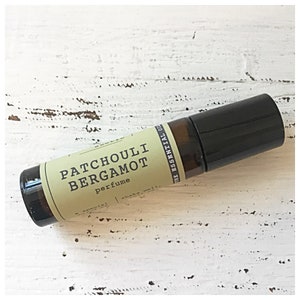 Puede incluir: Un frasco de vidrio marrón con tapa negra. La etiqueta dice "Patchouli Bergamot Perfume" con las palabras "Pure Essential Oils" impresas verticalmente en el lateral.