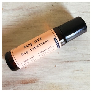 May include: A brown glass roll-on bottle with a black cap. The label reads "bug off bug repellent" and "a special blend of" with instructions to "shake well, roll on and massage".