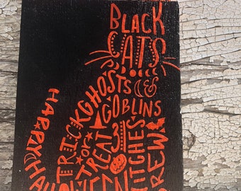 May include: Black wooden Halloween treat bag with an orange ribbon handle. The bag is decorated with orange text that says "Black Cats", "Trick or Treat", "Ghosts", "Goblins", "Witches", "Brew", and "Halloween".