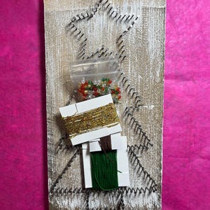 May include: A wooden Christmas tree craft kit with a star-shaped nail pattern. The kit includes a bag of colorful beads, gold thread, green thread, and brown thread.