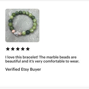 May include: A green marble bead bracelet with a silver Celtic knot charm. The bracelet is on a gray background.