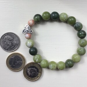 May include: A green jade stone bracelet with a silver Celtic knot charm. The bracelet is made of round beads and is about the size of a quarter.