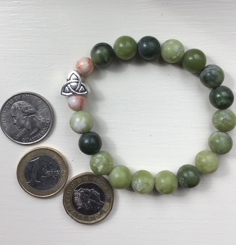 May include: A green jade stone bracelet with a silver Celtic knot charm. The bracelet is made of round beads and is about the size of a quarter.
