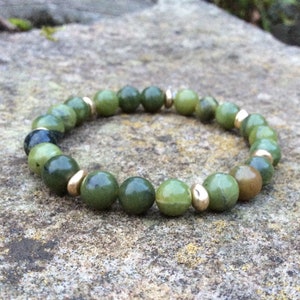 May include: A green jade bracelet with gold beads. The bracelet is made of round beads and is strung on a clear elastic cord.