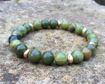 Pode incluir: Um bracelete de jade verde com contas douradas. O bracelete é feito de contas redondas e é enfiado em um cordão elástico transparente.