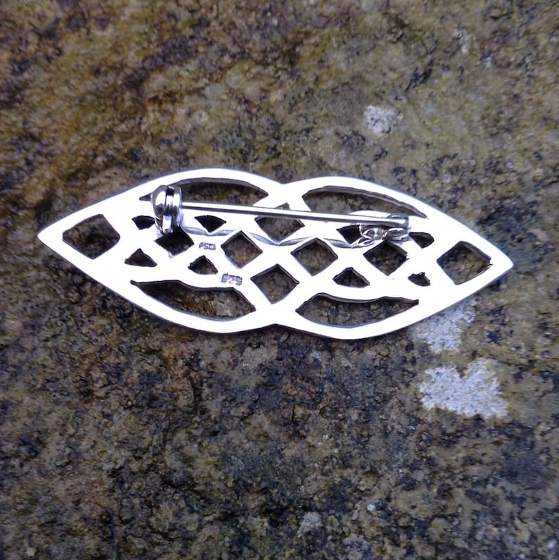 Pode incluir: Broche de n&oacute; celta de prata com um pino na parte de tr&aacute;s. A parte de tr&aacute;s da broche &eacute; marcada com os n&uacute;meros "925" e "079".