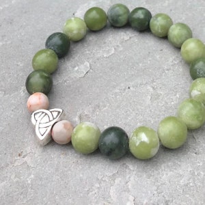 May include: A green and pink stone bracelet with a silver Celtic knot charm. The bracelet is made of round beads and is a popular style of jewelry.