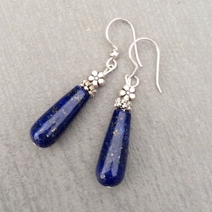 May include: A pair of silver dangle earrings with blue lapis lazuli teardrop stones and silver flower accents.