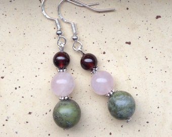 May include: A pair of silver dangle earrings with three beads each. The top bead is dark red, the middle bead is light pink, and the bottom bead is green with brown streaks.