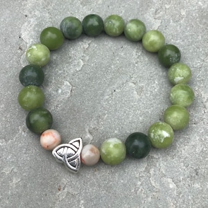 May include: A green jade stone bracelet with a silver Celtic knot charm. The bracelet has a graduated color scheme, with the stones getting darker green as they go around the wrist.