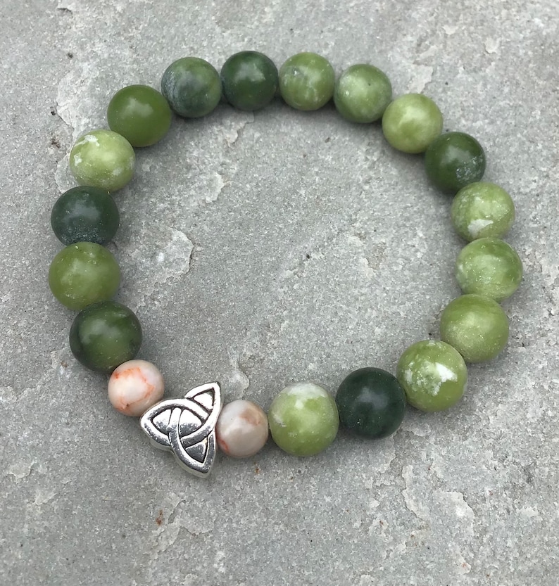 May include: A green jade stone bracelet with a silver Celtic knot charm. The bracelet has a graduated color scheme, with the stones getting darker green as they go around the wrist.