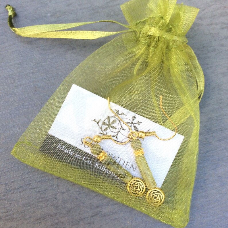 May include: A pair of gold earrings with Connemara marble beads and a Celtic knot design. The earrings are in a green organza bag with a white card that reads 'Made in Co. Kilkenny'.