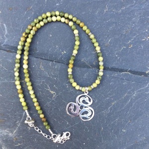 Puede incluir: Un collar de piedras verdes con un colgante de plata con un diseño de nudo celta. El collar está hecho de pequeñas cuentas redondas y tiene un cierre de plata.