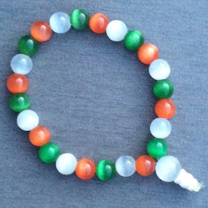 Könnte beinhalten: Ein Armband aus weißen, grünen und orangefarbenen Perlen. Die Perlen sind rund und haben eine glatte, polierte Oberfläche.