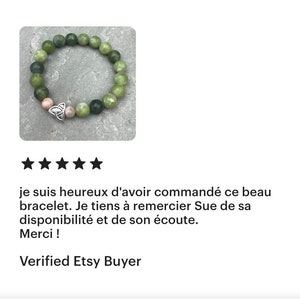 May include: A green and brown beaded bracelet with a silver Celtic knot charm. The bracelet is on a gray background.