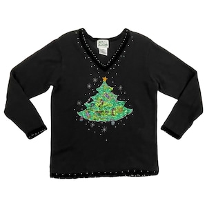 May include: Black long-sleeve sweater with a V-neck and a Christmas tree design. The tree is green with colorful ornaments and a gold star on top. The neckline and cuffs have a black velvet trim with small white embellishments.