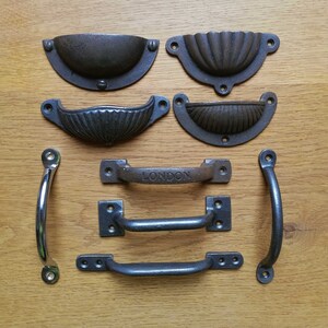 May include: Assortment of black cast iron drawer pulls and handles.  The handles feature a variety of styles, including a simple loop, a curved design, and a handle with the word "LONDON" on it.