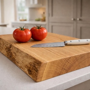 May include: A wooden chopping board with a natural edge, two red tomatoes and a knife with a white handle. The board is made of light brown wood and sits on a white countertop. Kitchenware.