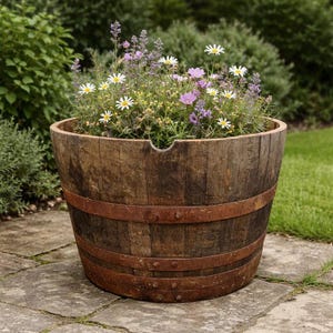 May include: A rustic wooden barrel planter, filled with a mix of flowers. The planter has metal bands and sits on a stone patio. The flowers include white daisies, purple blooms, and lavender. The planter is approximately 76 cm in diameter.