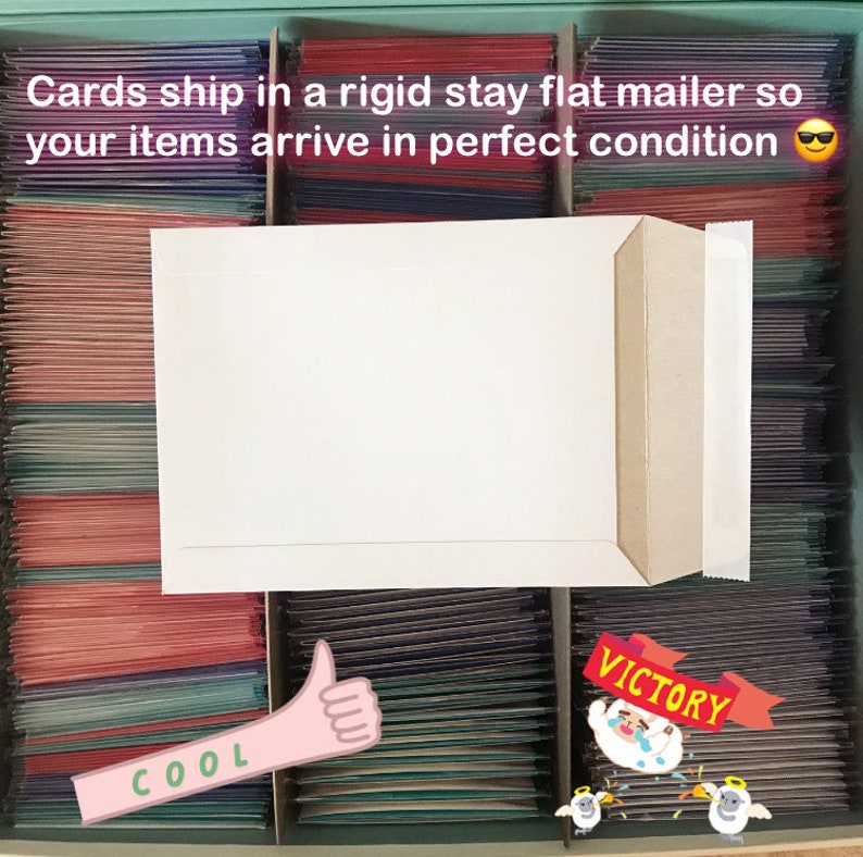 May include: A white rigid stay flat mailer with the text "Cards ship in a rigid stay flat mailer so your items arrive in perfect condition" and a smiley face emoji. The mailer is sitting on top of a drawer filled with colorful cards. The drawer has the words "COOL" and "VICTORY" written on it.