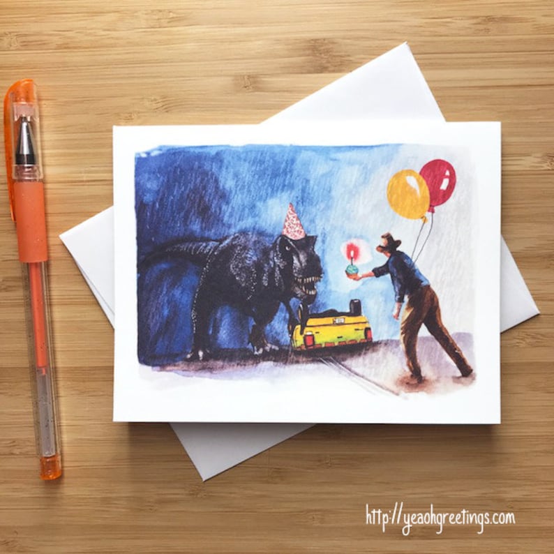 May include: Watercolor birthday card featuring a Tyrannosaurus Rex wearing a party hat, a person holding a lit candle, and balloons. The card has a blue background and a yellow vehicle. The pen is orange.