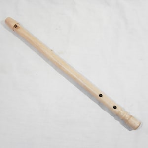 Puede incluir: Una flauta dulce de madera de color claro, un instrumento de viento, se encuentra en diagonal sobre una superficie blanca. La flauta dulce tiene una boquilla, agujeros para los dedos y un extremo acampanado. Se puede ver la veta de la madera.
