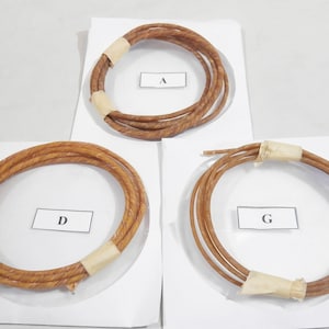 May include: Three bundles of brown, twisted rope, each coiled into a circle and secured with tan paper tape. Each bundle rests on a white sheet of paper with a lettered label.