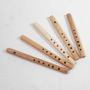 May include: Six wooden flutes of varying lengths, each with a different number of finger holes. The flutes are arranged in a fan shape on a white surface.