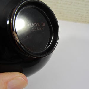 May include: A close-up shot of a black, glossy bowl. The base of the bowl has the text "MADE IN JAPAN" in a light brown colour. The bowl has a rounded shape and a small chip on the rim.