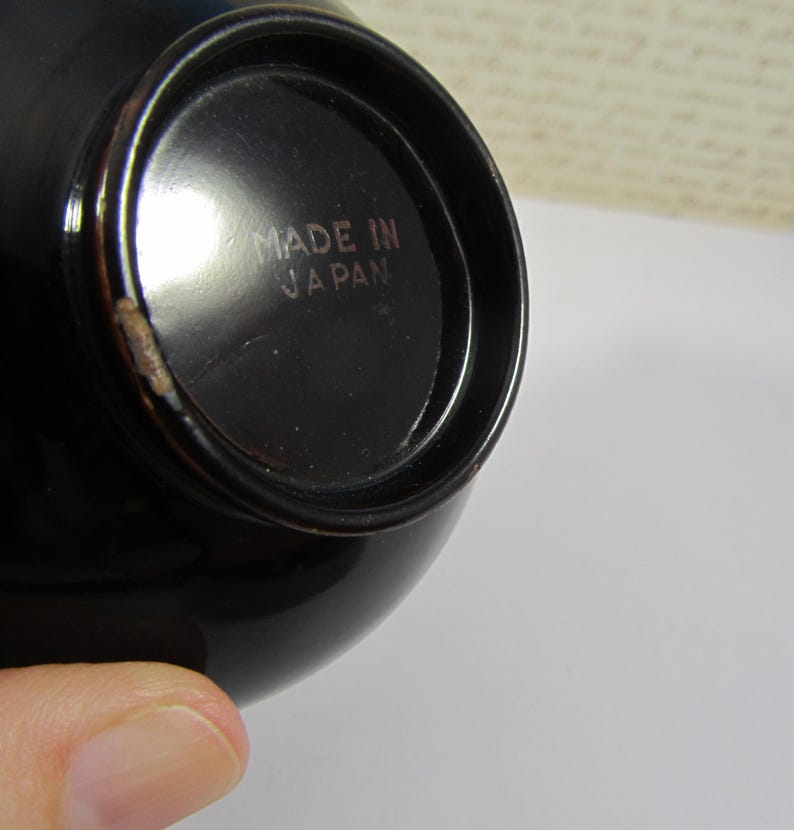 May include: A close-up shot of a black, glossy bowl. The base of the bowl has the text "MADE IN JAPAN" in a light brown colour. The bowl has a rounded shape and a small chip on the rim.