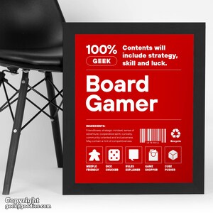 Pu&ograve; includere: Una stampa incorniciata con sfondo rosso e testo bianco che recita "Board Gamer". La stampa include il testo "100% GEEK" e "Contents will include strategy, skill and luck". Sotto ci sono icone e testo come "Meeple Friendly" e "Dice Chucker".