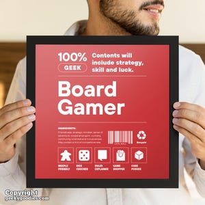 Pu&ograve; includere: Una stampa incorniciata con sfondo rosso e testo bianco che recita "Board Gamer". La stampa include il testo "100% I contenuti includeranno strategia, abilit&agrave; e fortuna" e icone di componenti di giochi da tavolo. La cornice &egrave; nera.