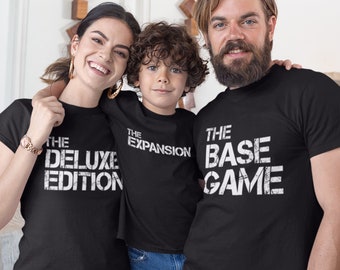 Puede incluir: Tres camisetas negras con texto blanco. Las camisetas dicen "The Deluxe Edition", "The Expansion" y "The Base Game".