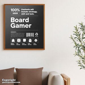 Pu&ograve; includere: Un poster incorniciato con sfondo nero e testo bianco che recita "Board Gamer". Il poster include il testo "100% GEEK" e "Contents will include strategy, skill and luck". Sotto ci sono icone e le parole "Meeple Friendly", "Dice Chucker", ecc.