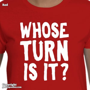 Può includere: T-shirt rosso con la scritta bianca "WHOSE TURN IS IT?". La maglietta è di colore rosso pieno e presenta un carattere semplice e in grassetto. Il testo è centrato sulla parte anteriore della maglietta.
