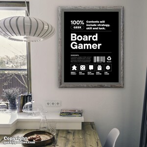Pu&ograve; includere: Un poster in bianco e nero incorniciato con la scritta "Board Gamer". Il poster include icone e le parole "Meeple Friendly", "Dice Chucker", "Rules Explainer", "Game Shopper" e "Cube Pusher".