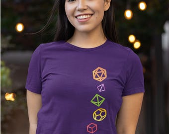 Puede incluir: Una camiseta morada con cuello redondo y mangas cortas, adornada con una serie de formas geométricas de dados de colores. La palabra "Purple" está en la parte superior izquierda. El texto "Copyright geekygoodies.com" está en la parte inferior izquierda.