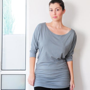 May include: A woman wearing a gray, long-sleeved, loose-fitting shirt with a scoop neck and black pants.