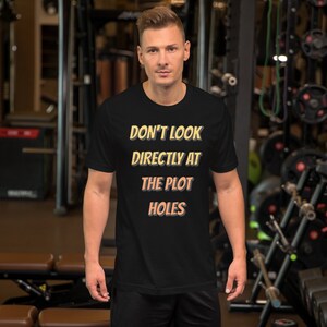 May include: A black t-shirt with the text "DON'T LOOK DIRECTLY AT THE PLOT HOLES" in yellow and orange letters.